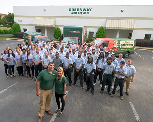 The full Mister Greenway Home Services team posing in front of company service vans at their headquarters.