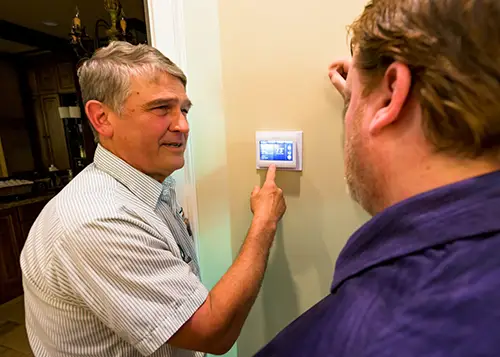 Mister Greenway technician demonstrating a programmable thermostat to a homeowner for improved energy efficiency and comfort.